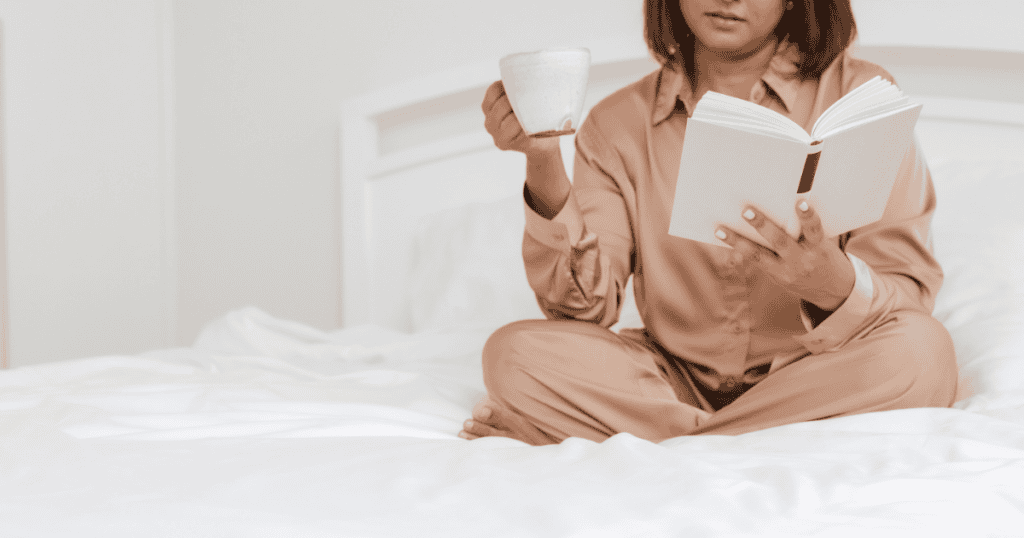 woman in bed reading her book and drinking coffee for her morning routine